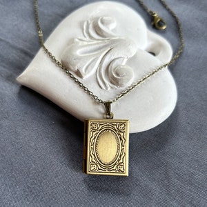 May include: A gold-toned locket necklace with a detailed, ornate design. The locket is shaped like a small book and has a hinged opening.