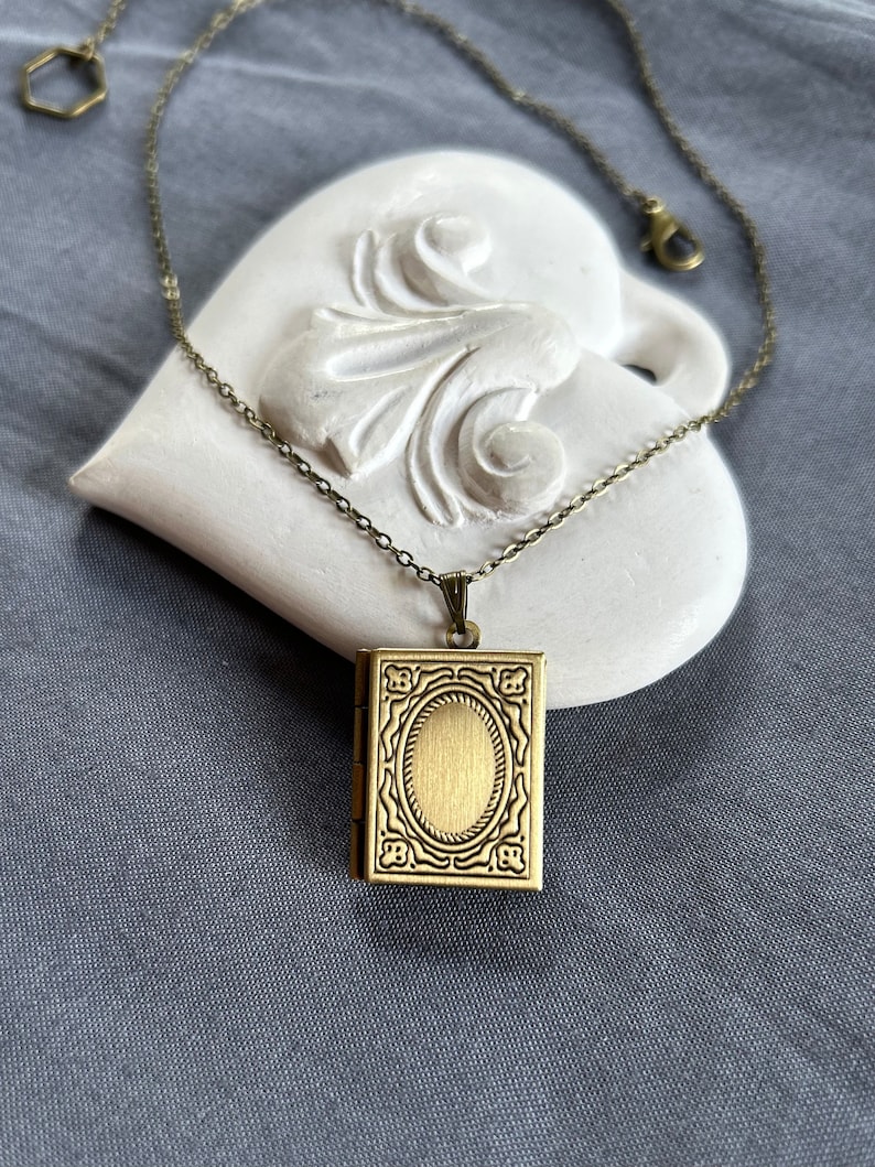 May include: A gold-toned locket necklace with a detailed, ornate design. The locket is shaped like a small book and has a hinged opening.