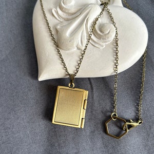 May include: A gold-toned locket necklace with a book-shaped pendant. The necklace has a delicate chain and a hexagonal clasp.