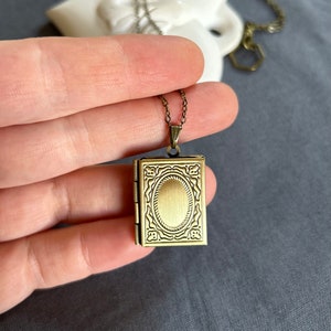 May include: A gold-toned locket necklace with an ornate design. The locket is shaped like a small book and has a hinged opening.