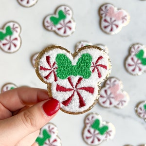 May include: A white felt Christmas ornament shaped like Mickey Mouse ears with a green bow and red and white candy cane designs.