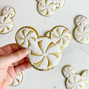 May include: Set of six white and gold felt Mickey Mouse head ornaments with a peppermint swirl design.