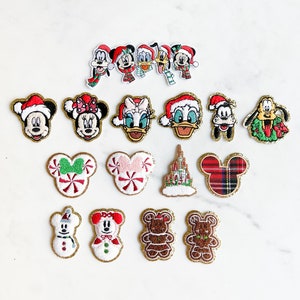 May include: A selection of Christmas-themed embroidered patches featuring Disney characters such as Mickey and Minnie Mouse, Donald Duck, and Pluto, all wearing festive hats. Other patches include gingerbread and castle designs.