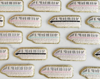 May include: A collection of 18 gold-trimmed embroidered patches featuring a white monorail train with different colored stripes. The patches are arranged in a grid pattern on a white background.