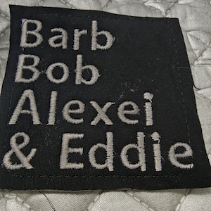 May include: Black fabric patch with white embroidered text that reads "Barb Bob Alexel & Eddie".