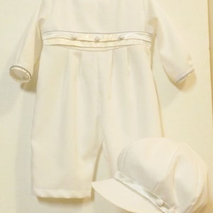 Pu&ograve; includere: Completo bianco per neonato con maniche lunghe e cappello bianco abbinato. Il completo &egrave; decorato con un nastro di raso bianco e bottoni perlati.