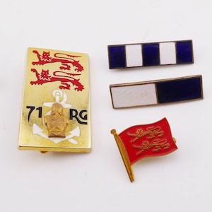 Puede incluir: Una colección de cuatro pines metálicos que incluye una insignia rectangular dorada con dos leones rojos, un ancla y el texto 71 RG, dos barras rectangulares con rayas de esmalte azul y blanco, y un pequeño pin de bandera roja con dos leones dorados.