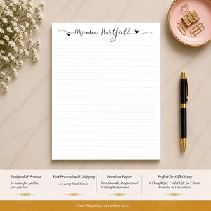 Op de afbeelding: Een wit gelijnd notitieblok met de naam "Monica Hartfield" in elegant schrift. Een zwarte pen met gouden accenten en een roze schaal met gouden paperclips zijn ook zichtbaar. Het notitieblok is ontworpen en gedrukt voor kwaliteit.
