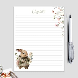 May include: Lined stationery with a watercolor illustration of a bunny wearing a coat and holding flowers. The name "Elizabeth" is written in cursive at the top. A white pen with a crystal-like design is on the right.