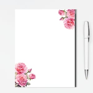 May include: White stationery paper with watercolor pink roses in the corners. A white pen rests on the right side of the paper. The roses have green leaves and are in full bloom.
