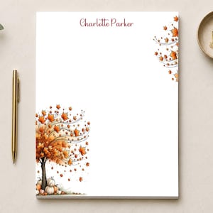 May include: A white rectangular notepad featuring the name Charlotte Parker in dark red script at the top. The design includes a watercolor illustration of a tree with orange autumn leaves and pumpkins at the base, plus falling leaves in the corner.