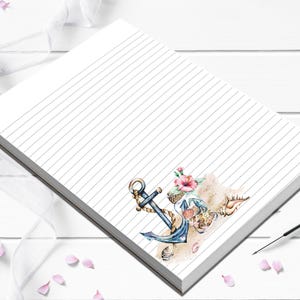 May include: A lined notepad with a nautical theme. The design features a blue anchor, seashells, and pink flowers on a sandy beach illustration. The notepad is white with gray lines.