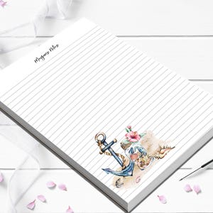 May include: A white lined notepad with the text "Megans Notes" in cursive. The bottom right corner features a watercolor illustration of a blue anchor, seashells, and pink flowers. The notepad is angled on a white surface.