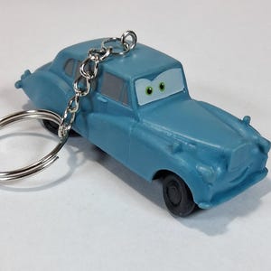 May include: A light blue toy car keychain with a silver keyring. The car has a cartoon face with green eyes and black tires. The keychain is a novelty item.