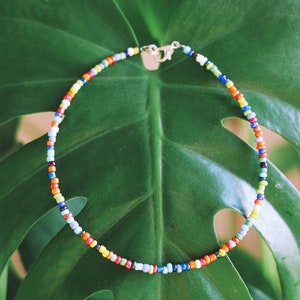 May include: A colorful beaded necklace with a silver clasp, resting on a green leaf.
