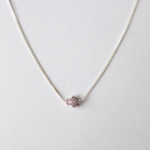 Pu&ograve; includere: Una collana a catena d'argento con un piccolo ciondolo rotondo. Il ciondolo &egrave; ricoperto di piccole pietre scintillanti.