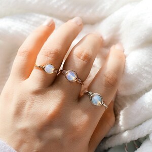May include: Three gold wire wrapped rings with opal stones. The rings are on a person's finger.