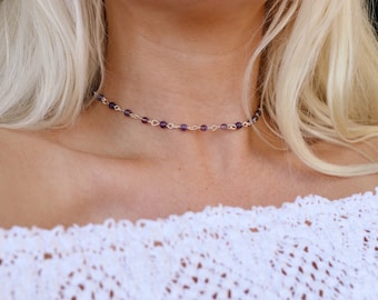 May include: A delicate silver chain necklace with small purple beads. The necklace is worn by a person with long blonde hair.