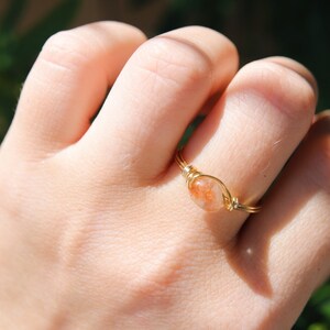 May include: A gold wire wrapped ring with a small, orange sunstone gemstone.