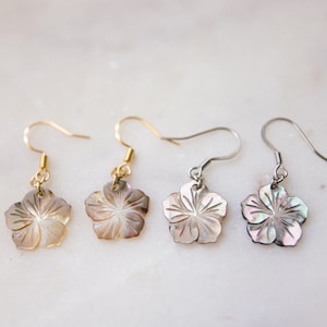 May include: Three pairs of earrings with a flower design made from mother of pearl. The earrings are available in gold, silver, and black.