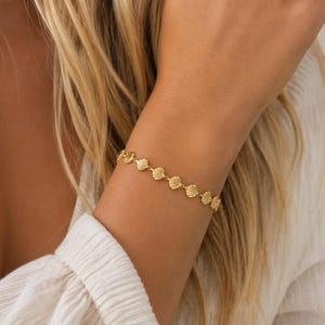 May include: A gold-toned chain bracelet featuring a series of small, uniform seashell-shaped charms linked together in a continuous row. The metallic links create a delicate, repeating pattern that encircles the wrist with a bright, polished finish.