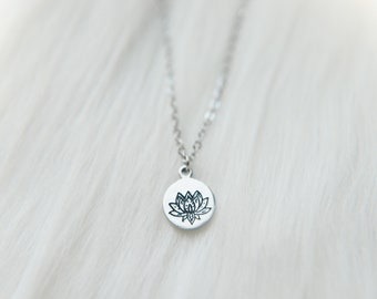 Op de afbeelding: Een zilveren ketting met een ronde hanger met een zwart lotusbloem ontwerp.