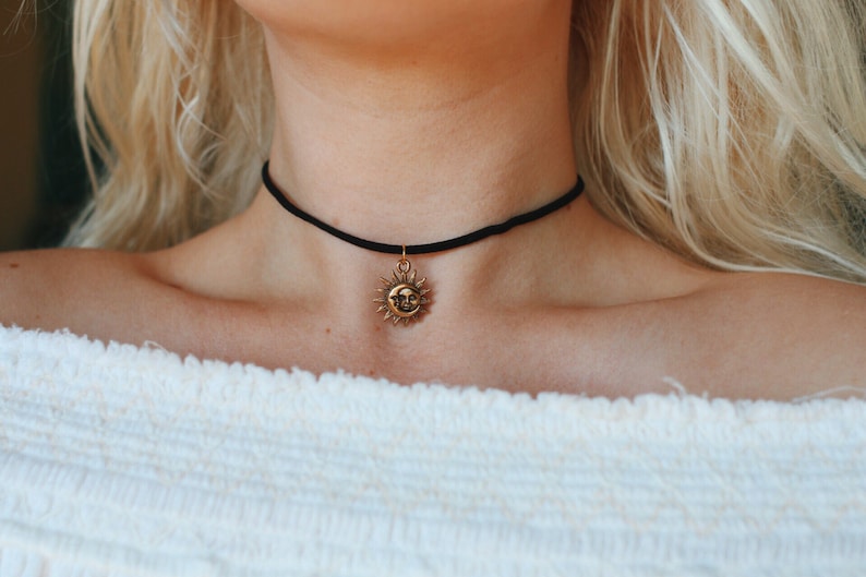 May include: A black choker necklace with a gold sun pendant. The sun has a face and rays.