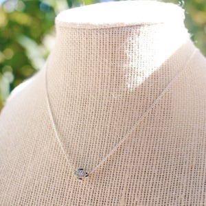 Pu&ograve; includere: Una collana a catena d'argento con un piccolo ciondolo rotondo. Il ciondolo ha un design testurizzato e geometrico.