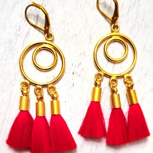 Peut inclure: Boucles d'oreilles créoles dorées avec trois breloques en forme de pompon rouge suspendues à chaque créole.