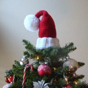 May include: A Christmas tree decorated with red and white baubles, a candy cane, and a white and red knitted Santa hat on top.