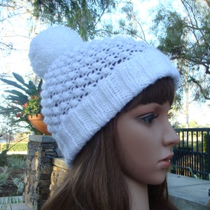 May include: White crocheted beanie with a large pom pom on top. The beanie has a textured stitch pattern.