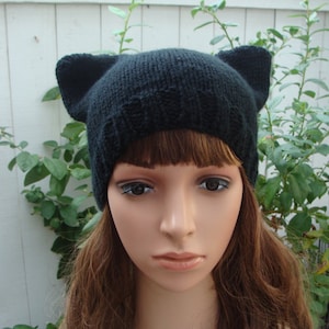 May include: Black knitted beanie with cat ears. The beanie is made from a soft, warm material and has a simple, stylish design.