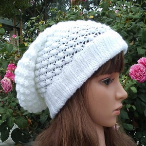 May include: White crocheted beanie with a textured, puffy design. The beanie is worn on a mannequin with long brown hair.