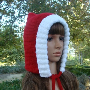 May include: Red and white knitted hooded hat with white pom-poms on the ends of the ties. The hat is made of soft yarn and has a cosy feel.