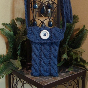 Peut inclure: Un sac à bandoulière en tricot bleu avec une fermeture à bouton blanc. Le sac est suspendu à un support en métal noir avec des éléments décoratifs.