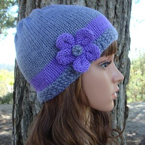 Puede incluir: Un gorro de punto gris y morado con un adorno de flor morada.