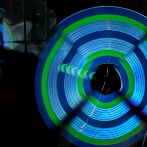 Può includere: Due oggetti circolari blu e verdi che ruotano su uno sfondo nero. Gli oggetti sono illuminati da luci blu e verdi, creando un effetto vorticoso.