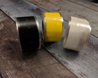 May include: Three rolls of tape, one black, one yellow, and one white. The rolls are on a wooden surface.