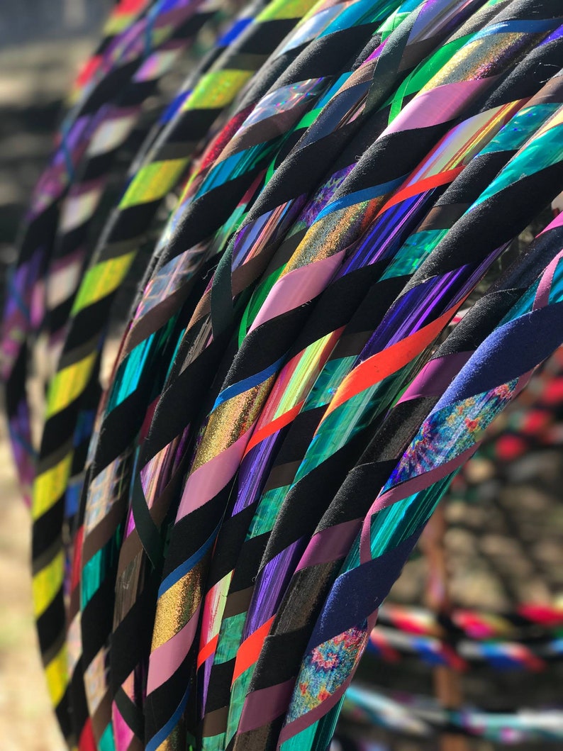 May include: A close-up of a stack of colorful hoops with black tape. The hoops are made of plastic and have a variety of colors, including green, blue, purple, and pink. The hoops are arranged in a diagonal pattern.