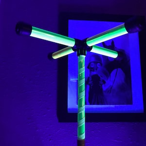 Può includere: Un apparecchio di illuminazione verde e bianco con quattro bracci che si estendono da un palo centrale. L'apparecchio è in una stanza con una parete blu e un quadro incorniciato sulla parete.