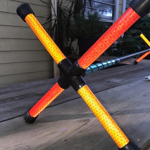 Puede incluir: Un poste de seguridad reflectante rojo y amarillo con un conector negro. El poste está hecho de un material ligero y está diseñado para ser duradero.