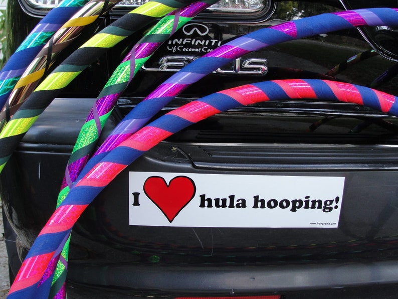 May include: A black car with a bumper sticker that says "I &hearts; hula hooping!"  The car is decorated with several colorful hula hoops, including green, yellow, purple, blue, and pink.