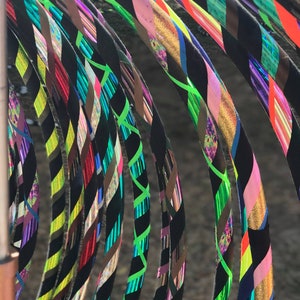 May include: A collection of colorful, patterned hula hoops with black tape. The hoops are arranged in a semi-circle, with the black tape facing the viewer. The hoops are made of a variety of materials, including plastic and metal.