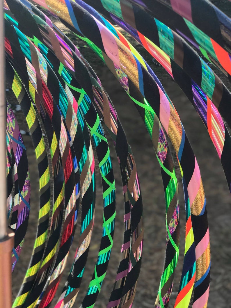 May include: A collection of colorful, patterned hula hoops with black tape. The hoops are arranged in a semi-circle, with the black tape facing the viewer. The hoops are made of a variety of materials, including plastic and metal.