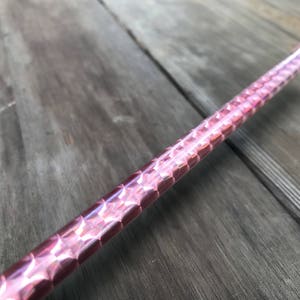 Può includere: Un'asta di vetro rosa con una superficie testurizzata. L'asta è composta da molti piccoli pezzi di vetro trasparenti e sfaccettati disposti in un motivo ripetitivo.