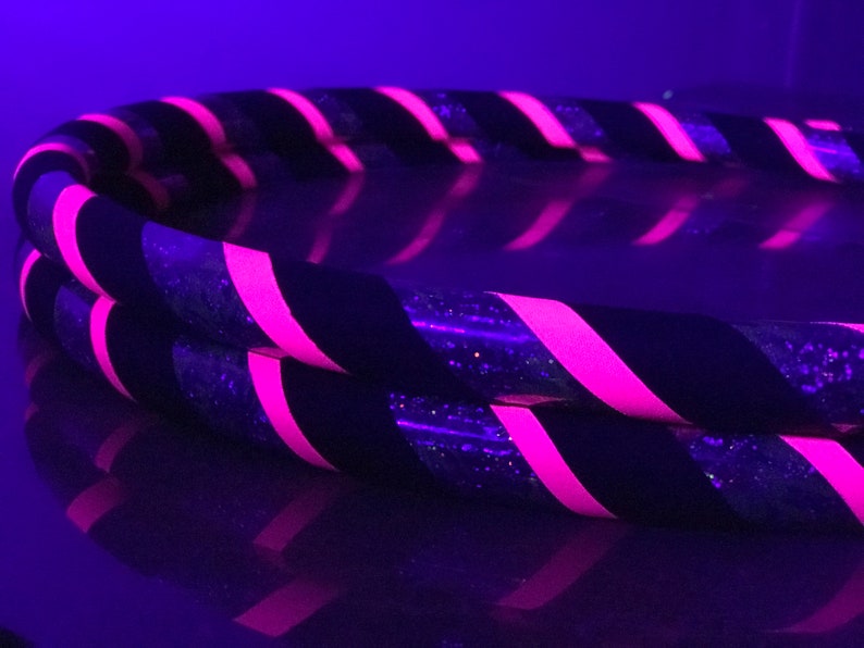 May include: Two black and pink striped hula hoops with glitter. The hoops are stacked on top of each other.