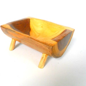 Puede incluir: Un peque&ntilde;o cuenco de madera con un acabado de madera natural. El cuenco est&aacute; tallado en una sola pieza de madera y tiene una forma &uacute;nica. Est&aacute; sostenido por cuatro peque&ntilde;as patas.