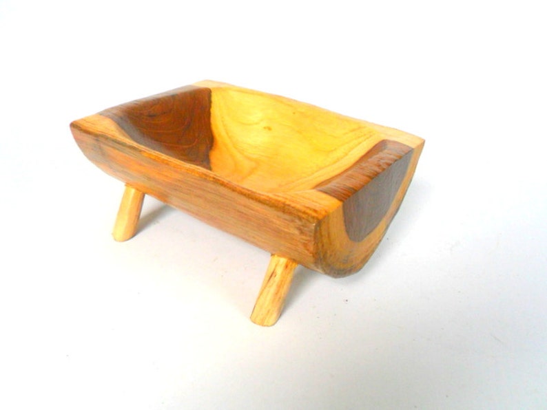 Puede incluir: Un peque&ntilde;o cuenco de madera con un acabado de madera natural. El cuenco est&aacute; tallado en una sola pieza de madera y tiene una forma &uacute;nica. Est&aacute; sostenido por cuatro peque&ntilde;as patas.