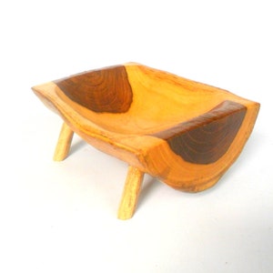 Puede incluir: Un peque&ntilde;o cuenco de madera con un acabado de madera natural y detalles en marr&oacute;n oscuro. El cuenco est&aacute; tallado en una sola pieza de madera y tiene cuatro patas.