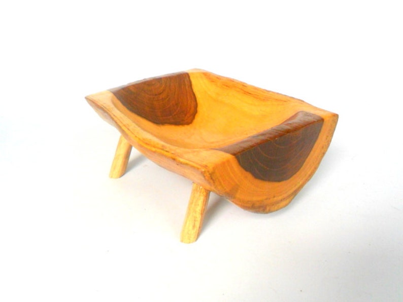 Puede incluir: Un peque&ntilde;o cuenco de madera con un acabado de madera natural y detalles en marr&oacute;n oscuro. El cuenco est&aacute; tallado en una sola pieza de madera y tiene cuatro patas.